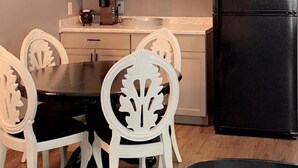 Una cocina compacta con armarios blancos, un refrigerador negro y una mesa de comedor con sillas blancas.