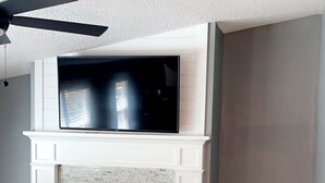Una sala de estar con chimenea, un televisor montado encima y un ventilador de techo.