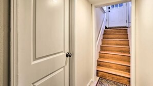 Een gang met een witte deur en een houten trap die leidt naar een kamer met witte wanden en een vloer met een patroon.