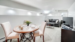 Een moderne woonkamer met een ronde eettafel, twee stoelen, een bank, een televisie en een klein bijzettafeltje.