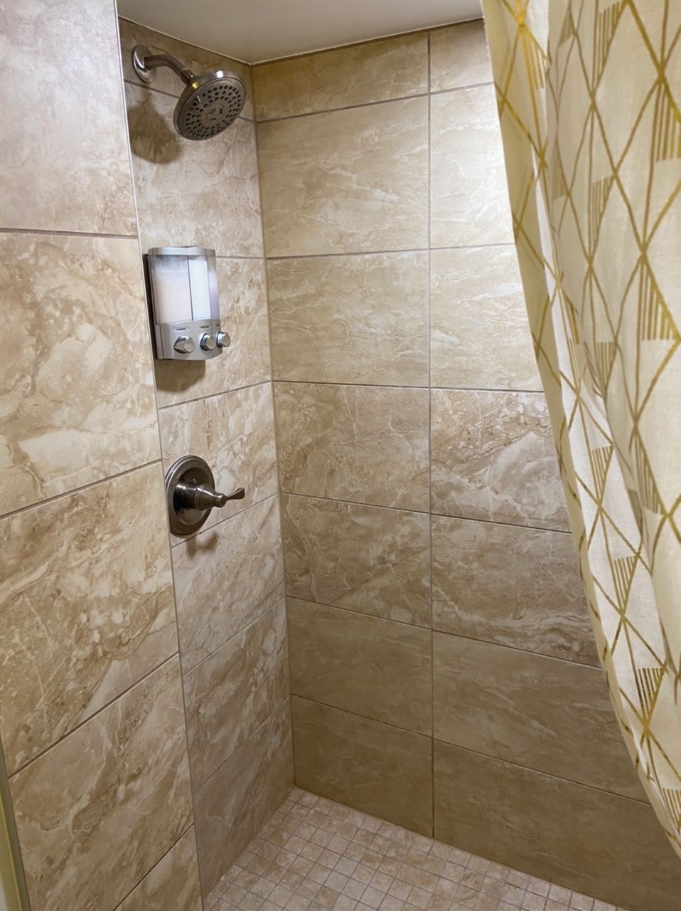 A shower area with a handheld showerhead, a wall-mounted control panel, and a door with a geometric-patterned curtain.