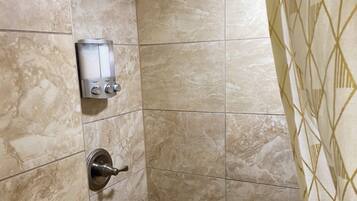 A shower area with a handheld showerhead, a wall-mounted control panel, and a door with a geometric-patterned curtain.