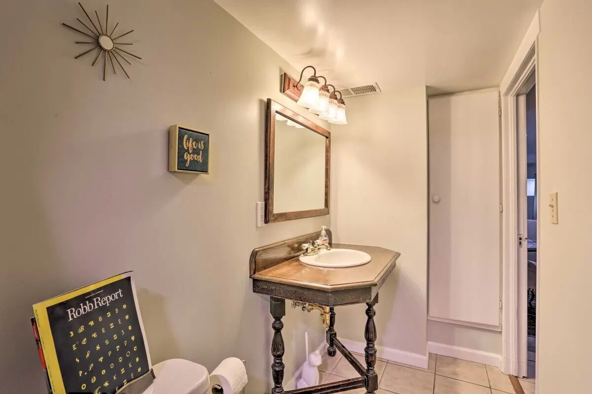 A bathroom with a vanity, sink, and mirror. There is a framed quote on the wall and a toilet paper holder.