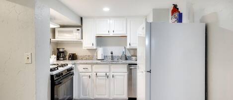 A compact kitchen with white cabinets, a stainless steel refrigerator, a stove, and a coffee maker.