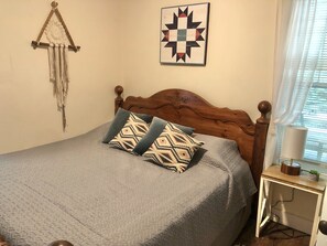 A neatly made bed with patterned pillows, a wooden headboard, a wall hanging, and a framed quilt. - Jocasee Landing Lake Cottage - 1 mi from boat ramp! (Salem)