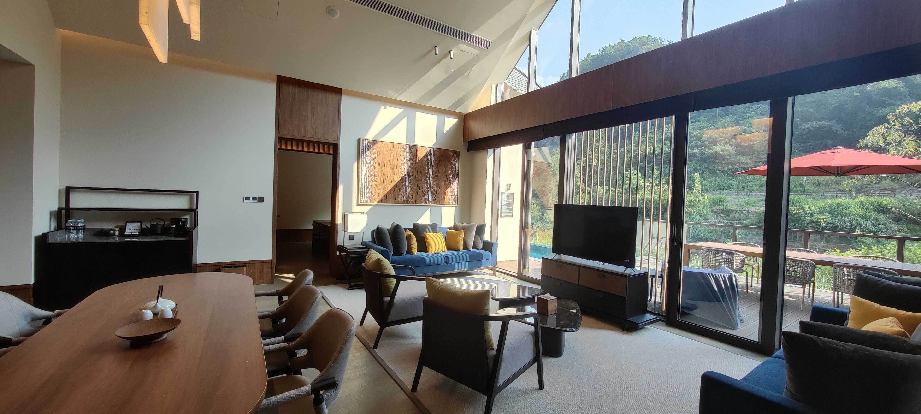 Una sala de estar moderna con una gran mesa de comedor, asientos cómodos, un televisor de pantalla plana y ventanas amplias que dan a vistas del exterior.