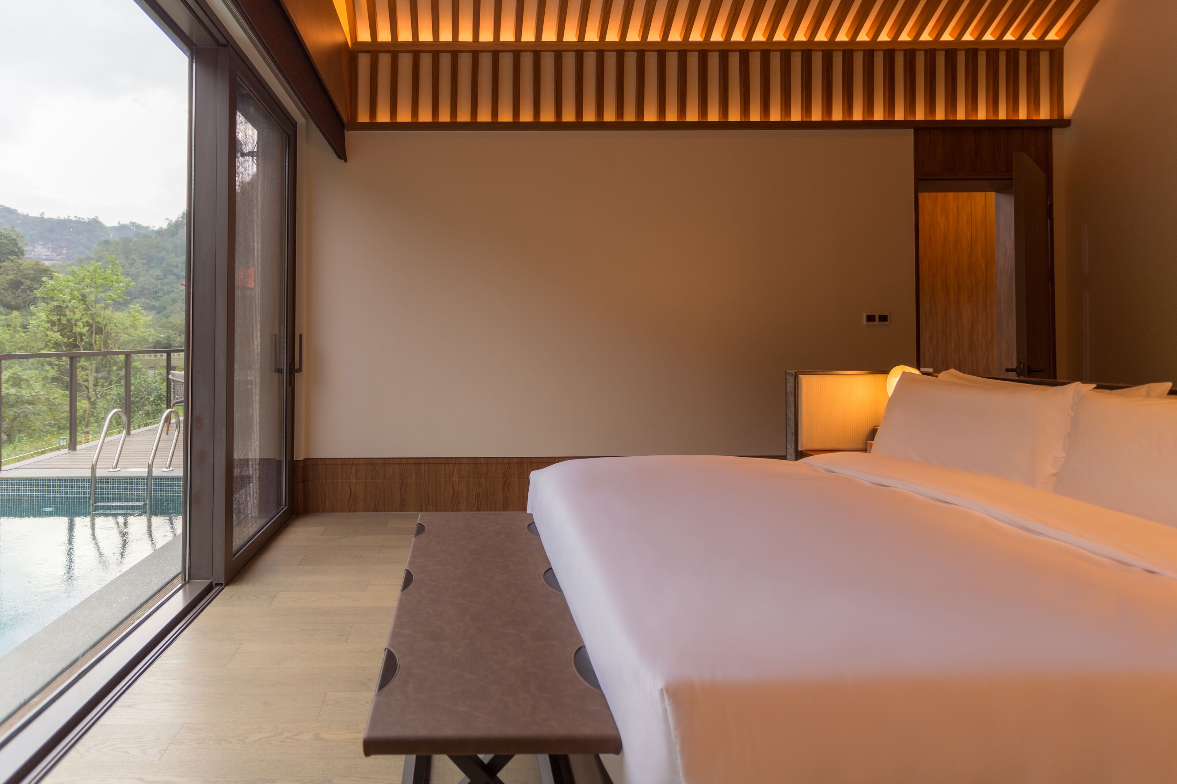 Un dormitorio con cama, una banca y vista a una piscina.