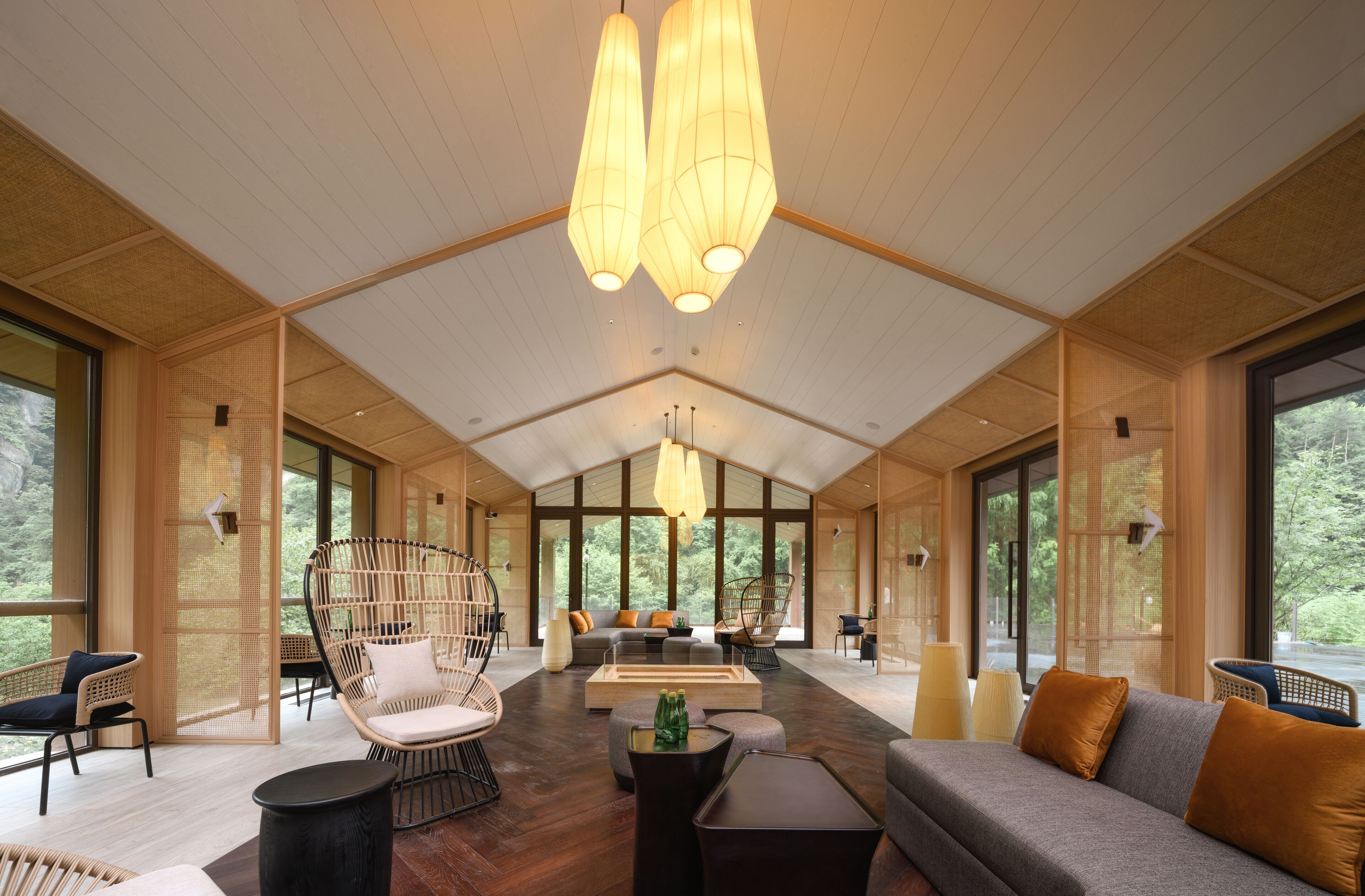 A spacious room with a high ceiling, large windows, and a central seating area with a sofa and chairs.