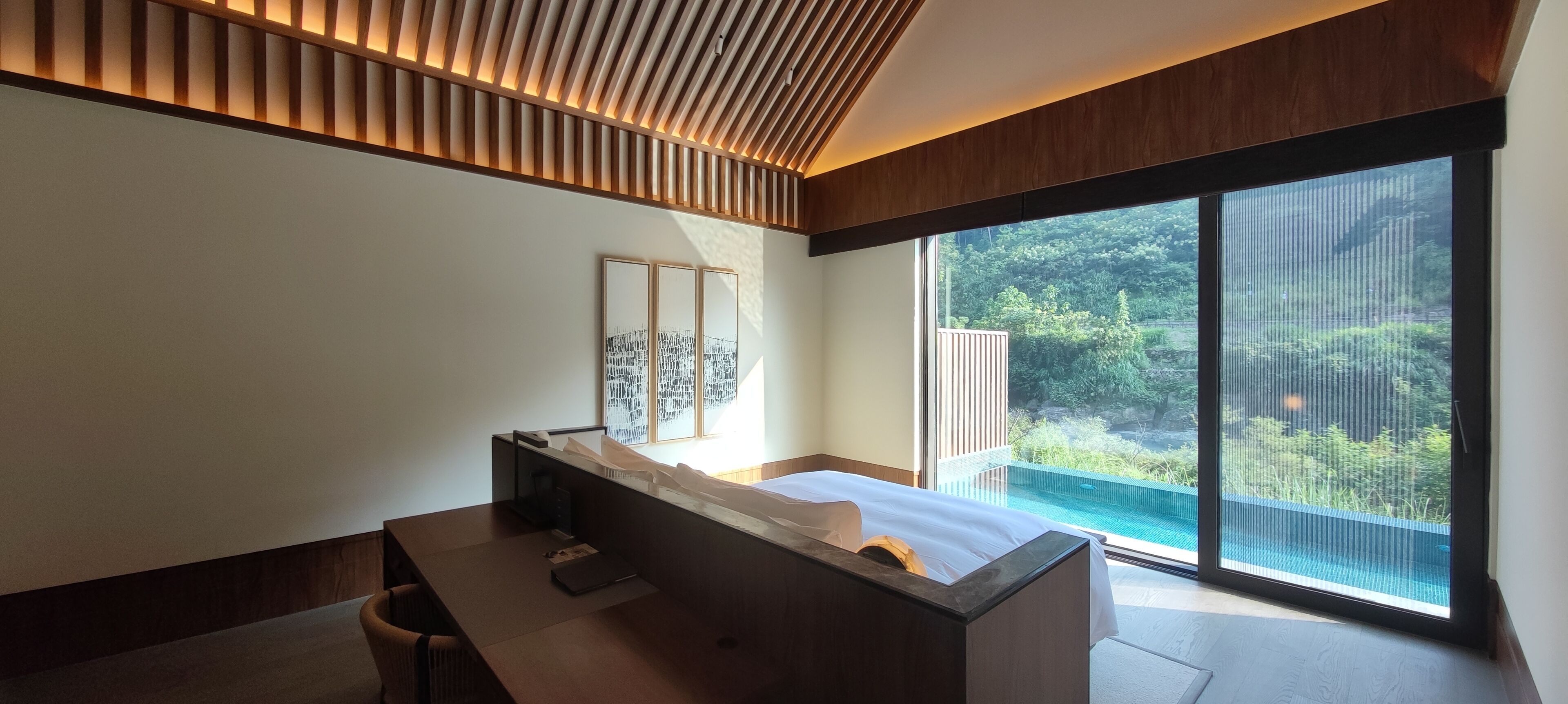 Un dormitorio moderno con una cama grande, un escritorio y vistas a una piscina y vegetación.