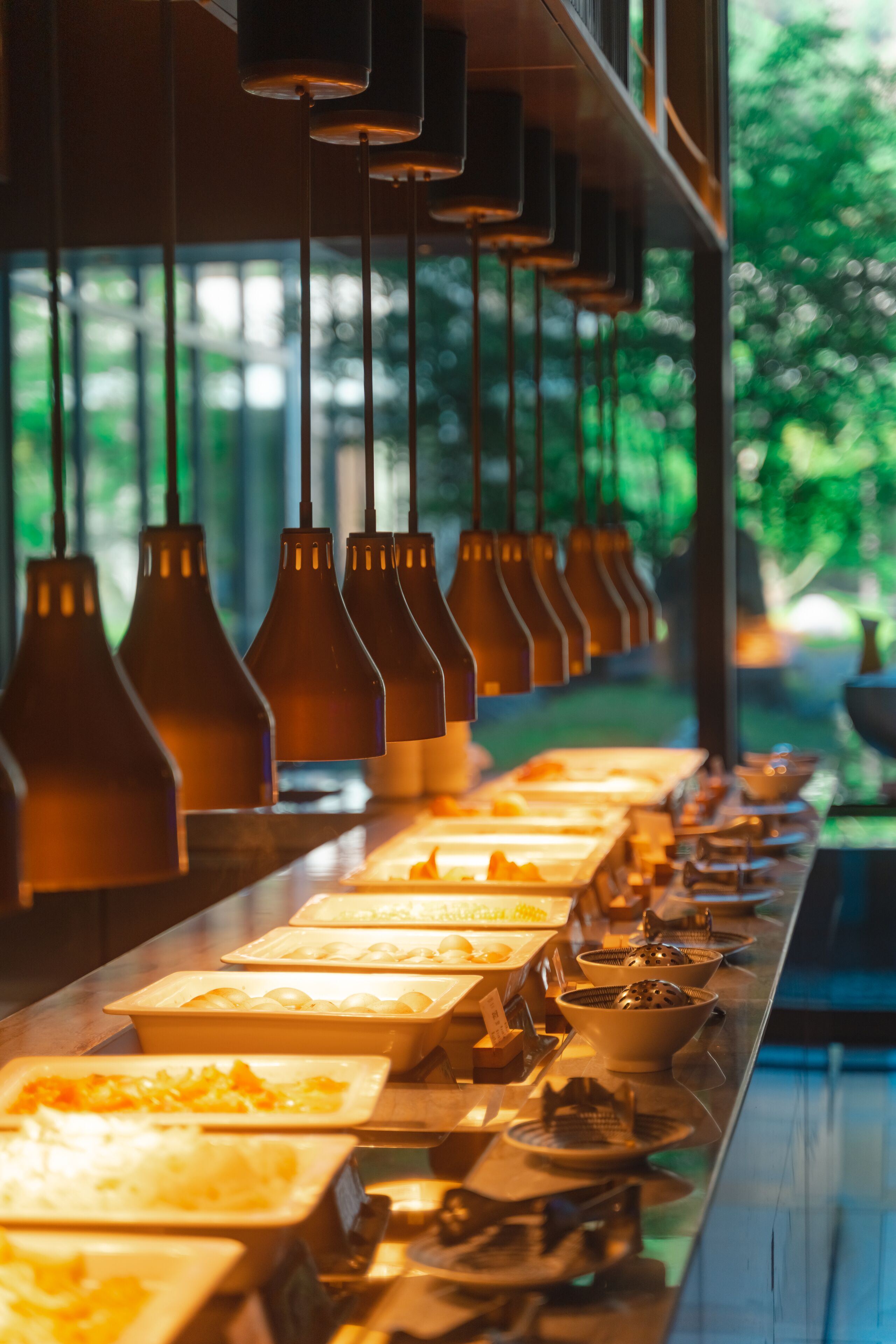 A buffet line with various food items and hanging pendant lights.