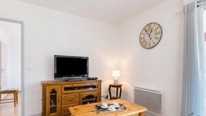 A living room with a television on a wooden cabinet, a table with cups and saucers, and a clock on the wall. - Côté du Lac by Interhome (Soustons)