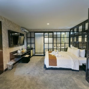 A hotel room with a bed, a desk with a flat-screen TV, a bathroom with a glass partition, and a large window. - Royal Regantris Cendana (Surabaya)