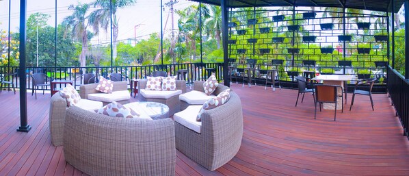 Relax in a serene outdoor space with wicker sofas and chairs surrounding a central table, offering a view of lush greenery through a patterned glass wall.