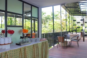 Un espacio al aire libre techado con una mesa lista para comer, sillas y vista a zonas verdes.