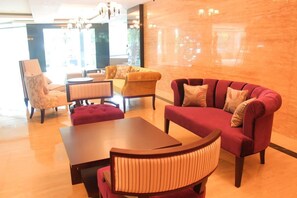 Eine Hotelhalle mit einem roten Sofa, einem gelben Sessel, einem Holztisch und einem gemusterten Sessel.