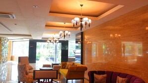 A modern hotel lobby with a seating area, chandeliers, and large windows. - Royal Regantris Cendana (Surabaya)