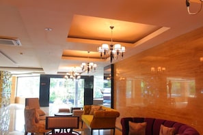 A modern hotel lobby with a seating area, chandeliers, and large windows.