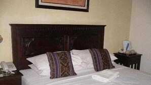 A hotel room with a bed, a nightstand with a phone, and a framed picture on the wall. - Royal Regantris Cendana (Surabaya)