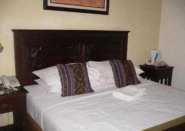 A hotel room with a bed, a nightstand with a phone, and a framed picture on the wall.