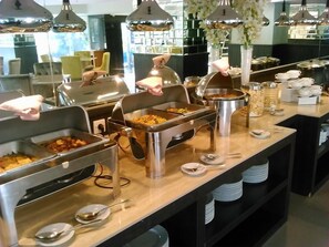 Ein reichhaltiges Buffet mit mehreren Speiseauslagen, Edelstahl-Serviergeschirr und verschiedenen Besteck.