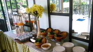 A buffet setup with glassware, plates, and a vase of yellow flowers. - Royal Regantris Cendana (Surabaya)