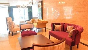 A hotel lobby with a red sofa, a yellow armchair, a wooden table, and a patterned armchair. - Royal Regantris Cendana (Surabaya)