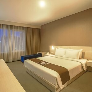 Habitació d'hotel amb un llit gran, una tauleta de nit, una cadira i una finestra amb cortines.