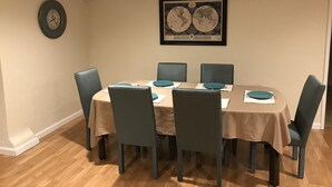 Een eetkamer met een ronde tafel, zes stoelen en een klok aan de muur.