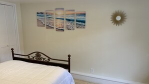 Een slaapkamer met een bed, een zon decoratie aan de muur en een reeks schilderijen met een strandthema.