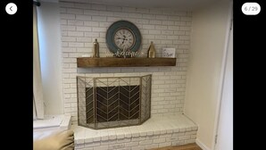 Een wit metselwerk schoorsteen met een decoratief metalen rooster, een klok en een plank met een 'Welcome' bord erboven.