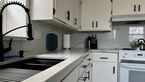 Een keuken met witte kastjes, een roestvrijstalen spoelbak, een waterkoker en een fornuis.