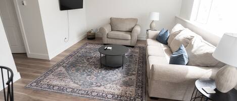 A living room with a beige sofa, a black coffee table, and a patterned rug.