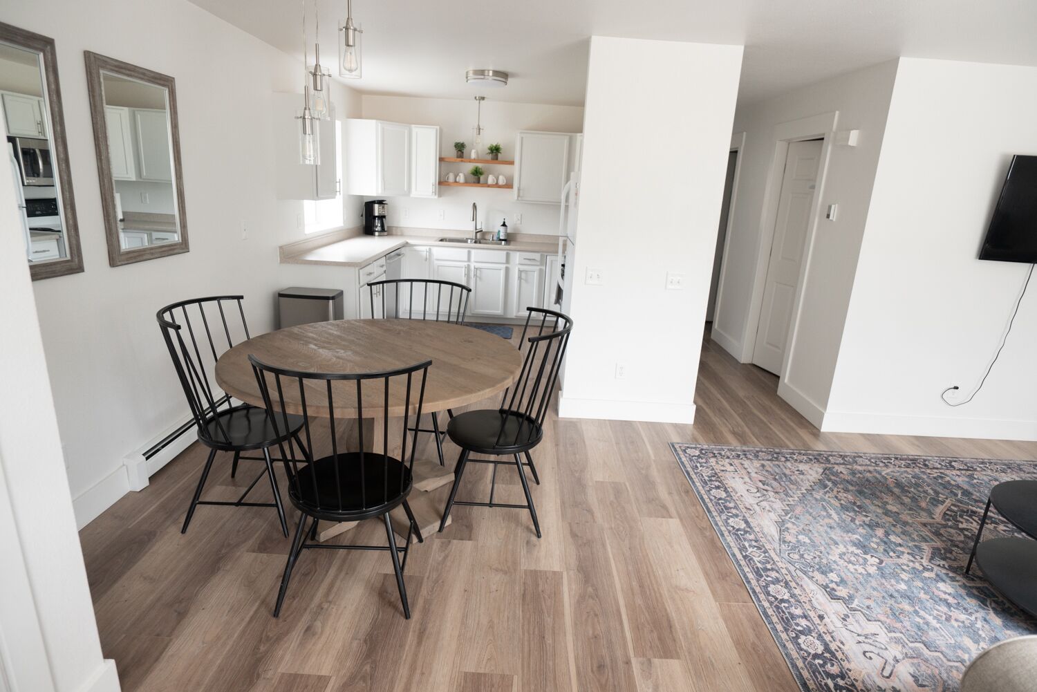A modern kitchen with white cabinets, a round wooden table with chairs, and a kitchen island.