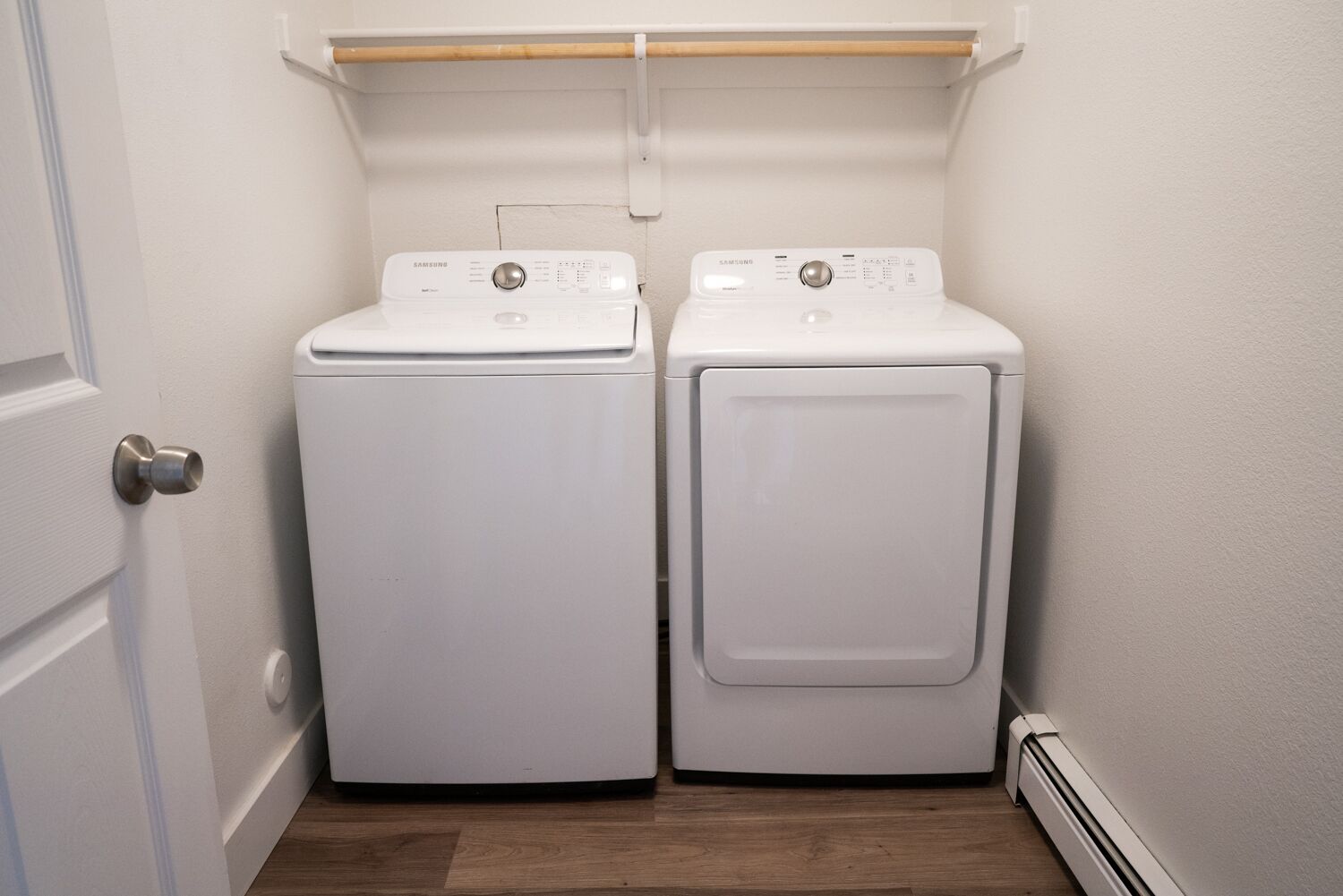 Une buanderie équipée de deux machines à laver à chargement frontal, de couleur blanche, et d’une étagère en bois placée au-dessus.