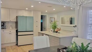 A modern kitchen with white cabinetry, a teal refrigerator, and a dining area with a table and chairs. - Cape Cod Sunscape. Orleans (Orleans)
