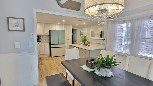 A modern kitchen with white cabinets, a two-door refrigerator, and a dining area with a dark table and chairs. - Cape Cod Sunscape. Orleans (Orleans)