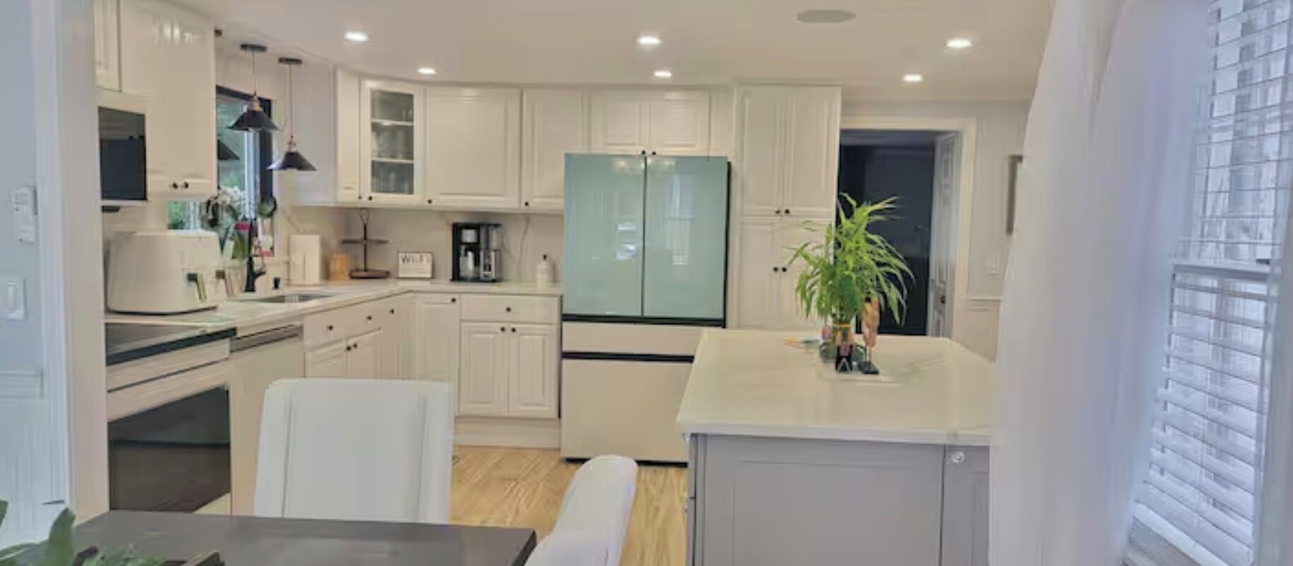 A modern kitchen with white cabinets, a refrigerator, and a dining area with a table and chairs.