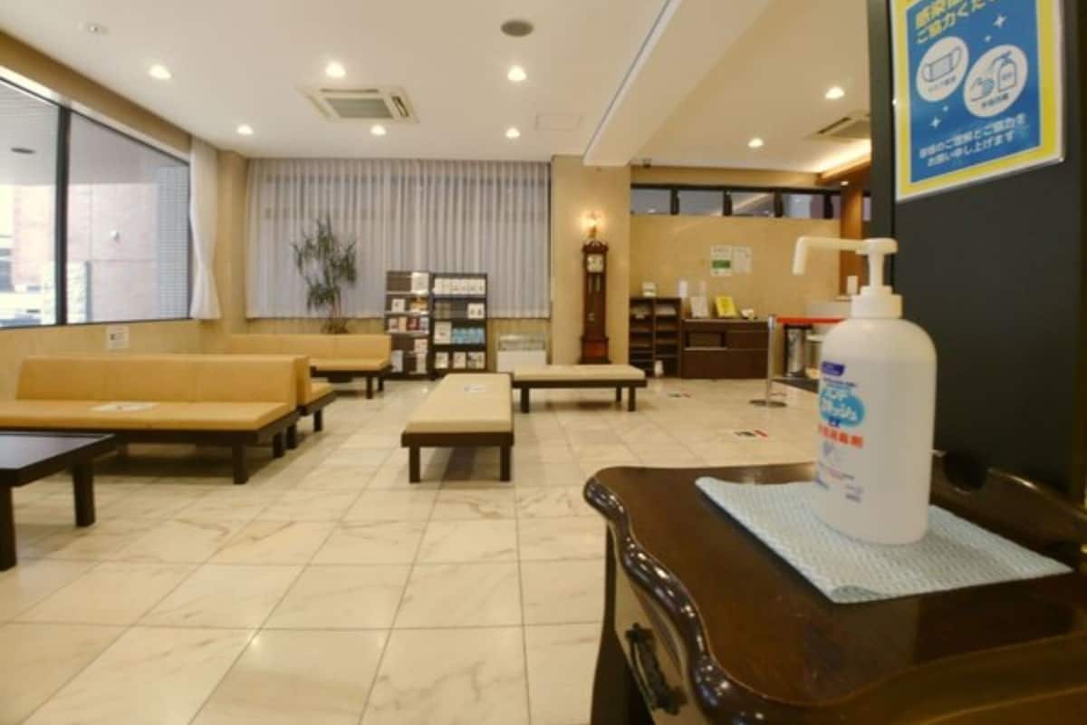 A hotel lobby with seating, a reception desk, a clock, and a poster on the wall.