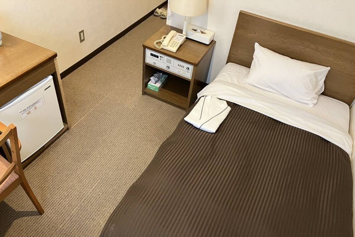Ein Hotelzimmer mit einem Bett, einem Nachttisch mit Telefon und Lampe, einem Schreibtisch mit Kühlschrank und einem Sessel.