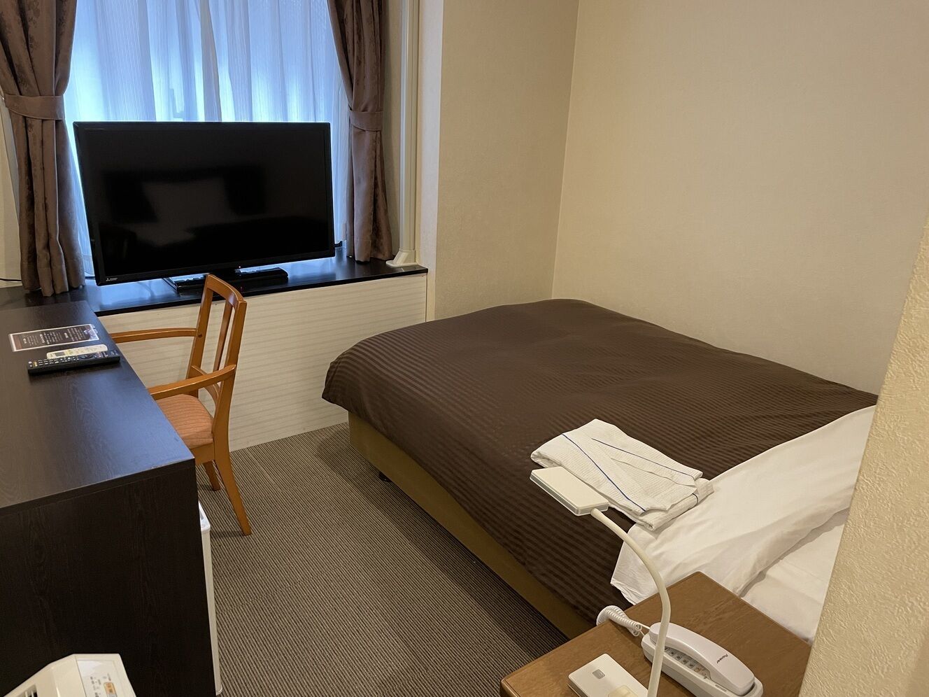 Ein Hotelzimmer mit Bett, Schreibtisch, Stuhl, Fernseher und einem fensterbepflanzten Fenster.