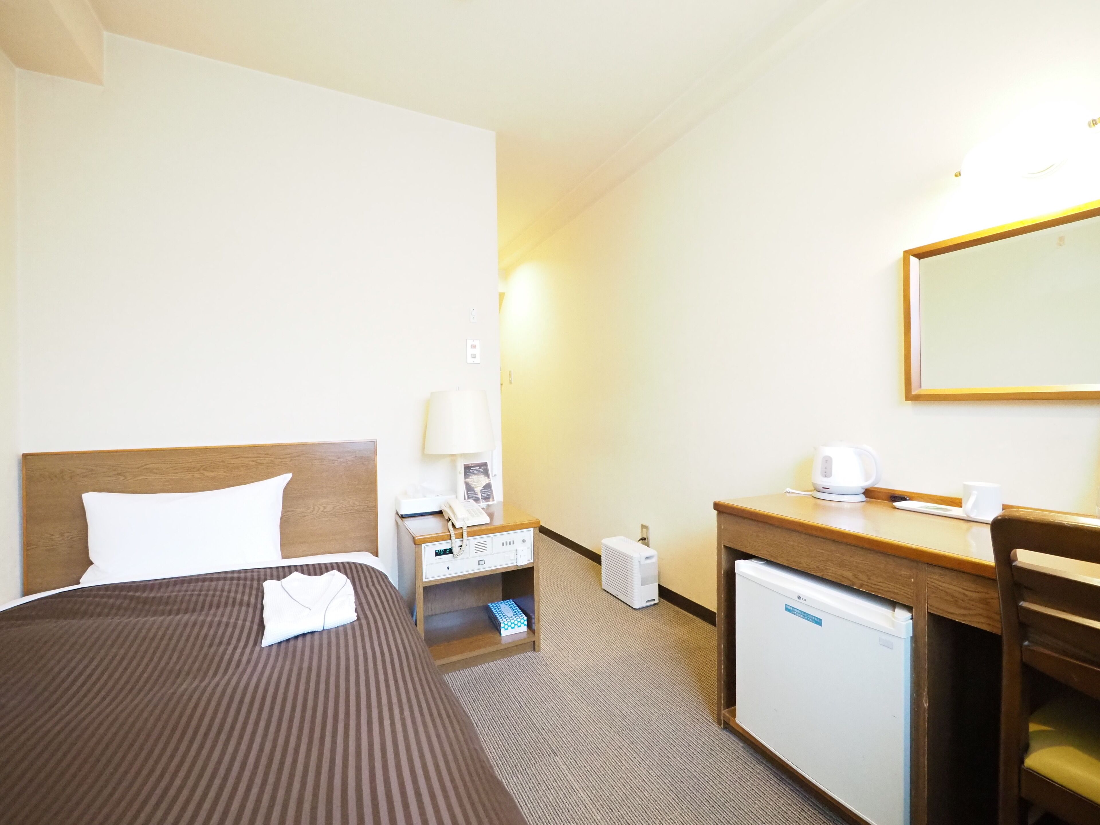 Ein Hotelzimmer mit Bett, Nachttisch, Lampe, Schreibtisch, Stuhl und kleinem Kühlschrank.