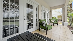 A covered patio area with a black bench, green cushioned chairs, and a tiled floor.