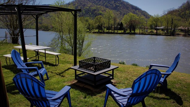 Un área de descanso junto al lago con sillas Adirondack, una mesa y un brasero.