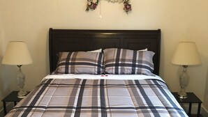 Una cama con colcha escocesa, dos lámparas de noche y un adorno floral en la pared.