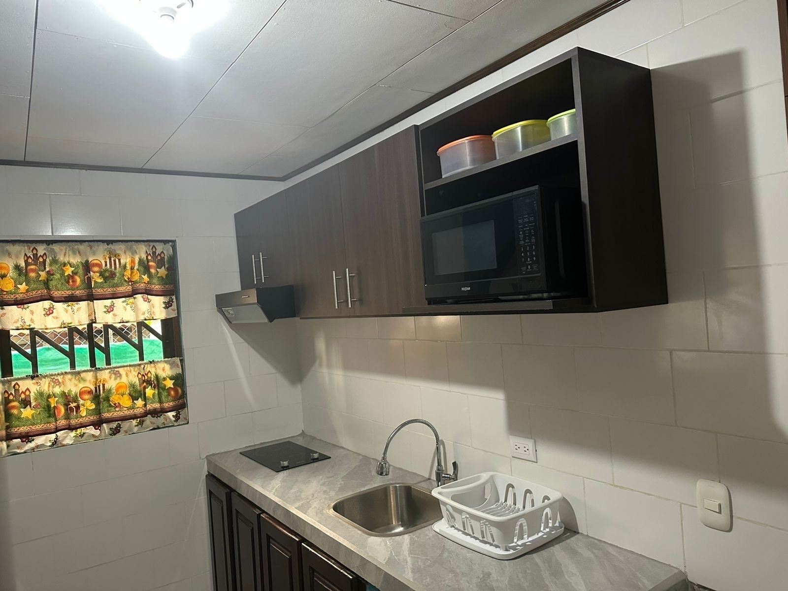 Een keuken met donkere houten kastjes, een ingebouwde magnetron, een roestvrijstalen spoelbak en een decoratief wandobject.