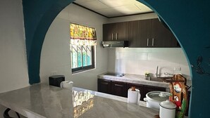 Une cuisine dotée d’un plan de travail en marbre, de meubles de couleur sombre, d’une fenêtre ornée de vitraux et d’une figurine décorative en bois.