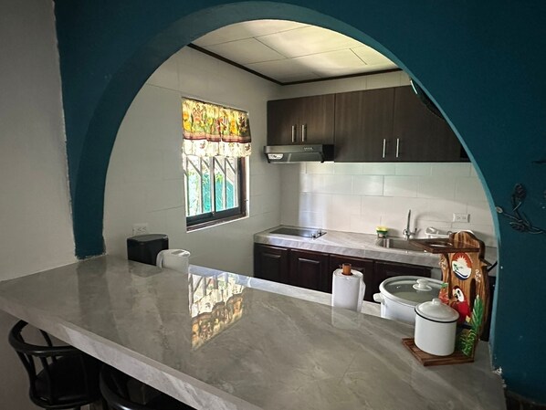 A kitchen with a marble countertop, dark cabinets, a window with a stained glass design, and a decorative wooden figure.