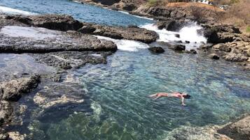 Un plan d’eau aux eaux claires, parsemé de formations rocheuses, où une personne est en train de nager.