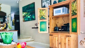 A living room with a wooden cabinet, a glass coffee table with a flower vase, and a painting of a pond on the wall. - 2 connected villas 19 Pax (Playa del Carmen)