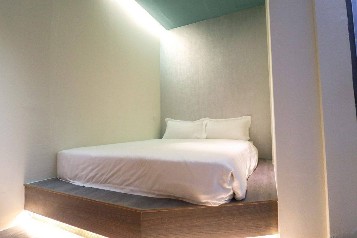 A minimalist bedroom with a bed, a wooden platform, and a sloped ceiling.